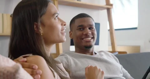 Couple on sofa at home, man leaning back speaking, holding tablet, woman Stock Footage 337745270