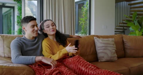 Couple on sofa smiling, navigating TV menu using black remote while selecting Stock Footage 313957071