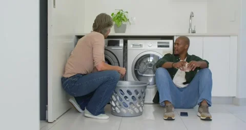 Couple sorting laundry in laundry nook, woman loading washer from basket, man Stock Footage 336569634
