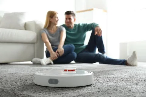 Couple spending time together while robotic vacuum cleaner doing its work at  Stock Photos