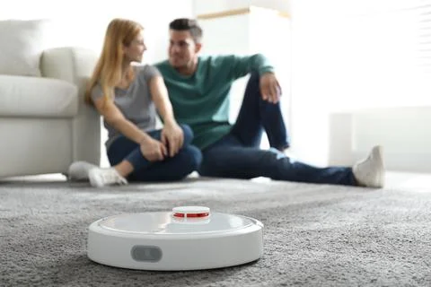 Couple spending time together while robotic vacuum cleaner doing its work at  Stock Photos