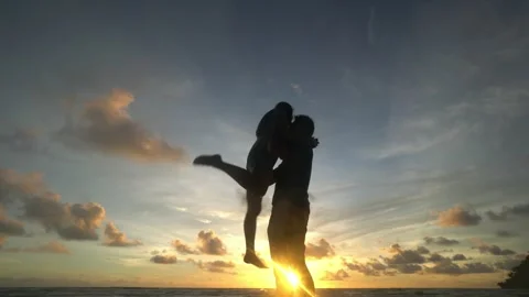 Couple stand on a beach at sunset, looking out at the ocean Stock Footage 313555640