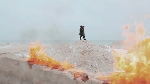 Couple standing against a background of fire, on the hill of sand. Winter sea Stock Footage 70994282