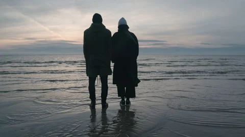 A couple standing and looking towards ocean on the cold beach Stock Footage 143253348