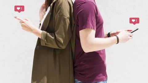 Couple standing back back using cellphone with love messages icons against wall Stock Photos