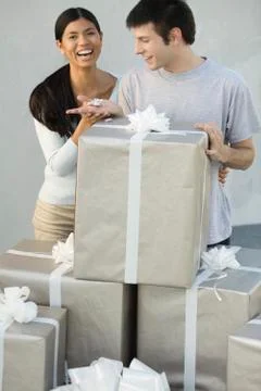 Couple standing behind stack of large gift boxes, man holding tiny present, Foto stock