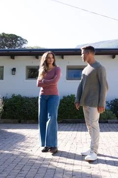 Couple standing facing one another on paved yard by house with lantern, wearing Stock Photos