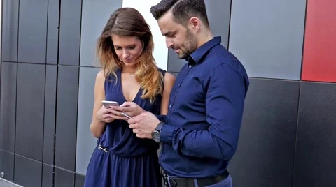 Couple  standing in front of modern building. They are using mobile phones. Stock Footage 55390891