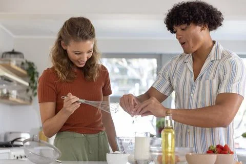 Couple standing in kitchen preparing batter, woman holding whisk over glass Fotos Stock