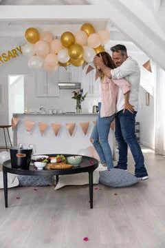 Couple standing in open-plan kitchen celebrating with gold balloons snacks on Fotos Stock