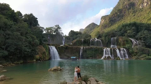 Couple Standing on Rocks in Front of Monumental Ban Gioc Waterfalls Aerial Drone Stock Footage 125498057