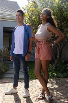 Couple standing on sunlit paved pathway by house, wearing casual summer clothes, Fotos Stock