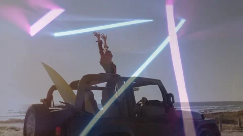 Couple standing through open-top Jeep at beach parking, raising arms, surfboard Stock Footage 333351393