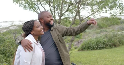 Couple standing by tree at dunes, man in olive jacket spotting and pointing Stock Footage 339513197