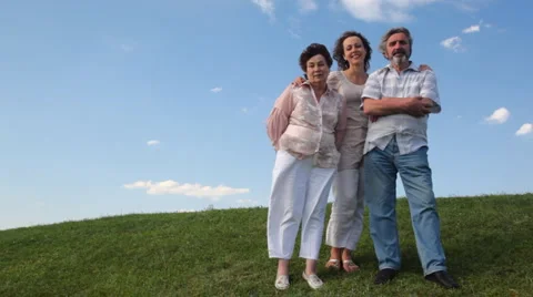 Couple stands embracing with adult daughter on grass Stock Footage