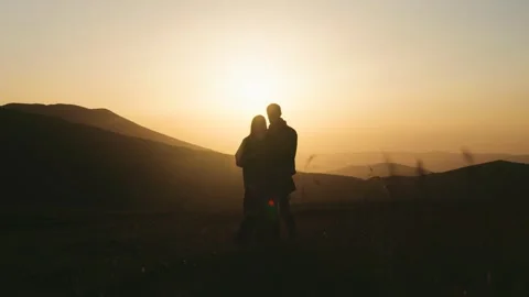 Couple stands together during sunset with mountains in background and horizon gl Stock Footage 343843300