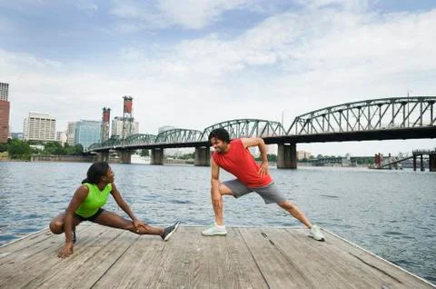 Couple stretching on urban boardwalk along river Stock Photos