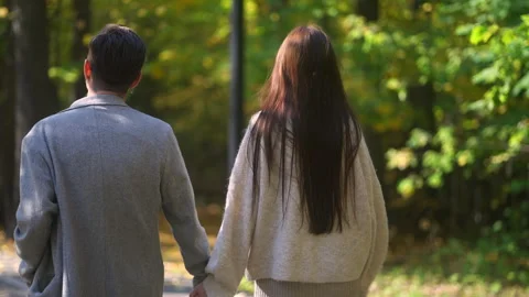 A couple strolling hand in hand through a serene, beautiful park filled with Stock Footage 288435719