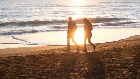 A couple strolls along the beach at sunset Stock Footage