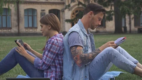 Couple of students sits back to back on the lawn Stock Footage 79676397