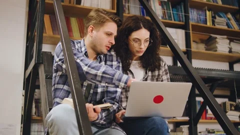 Couple studies together in a library while sitting on steps during the afternoon Видео 323937929