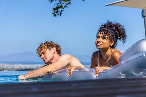 Couple sunbathing on silver raft in infinity pool, man bare-chested woman in 写真素材