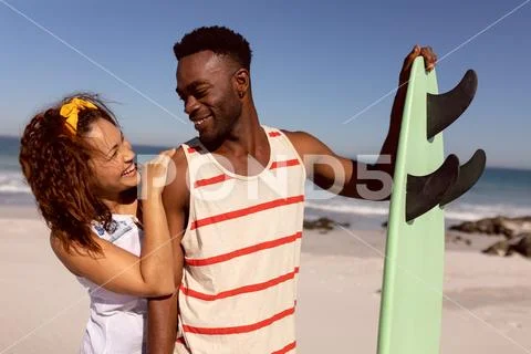 Couple with surfboard looking each other on beach in the sunshine Stock Photos