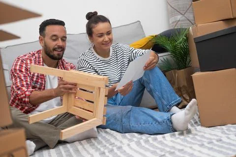 A couple, surrounded by moving boxes, assembles a DIY shelf, customizing their Stock Photos