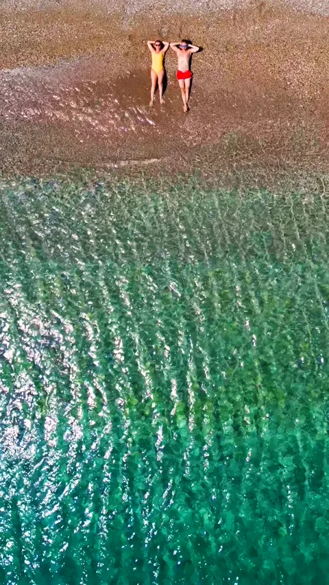 Couple in swimsuits lay on a sandy beach, top down view. Vertical Video stock 339629027