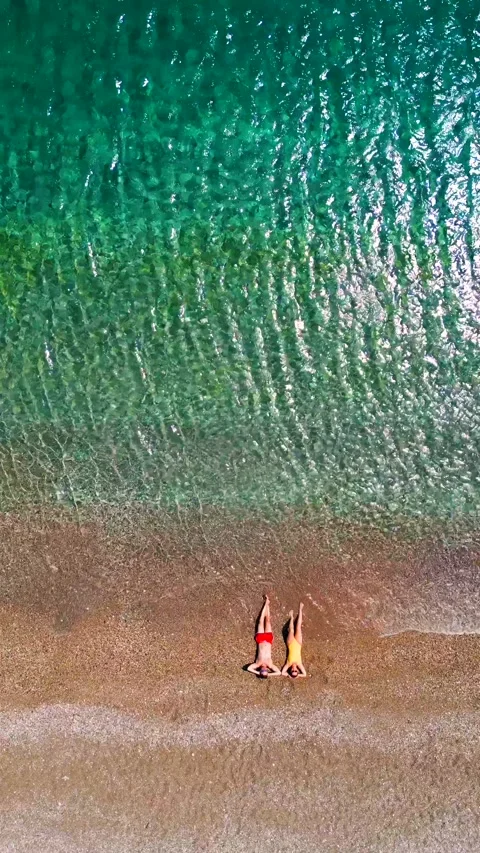 Couple in swimsuits lay on a sandy beach, top down view. Vertical 動画素材 341975946