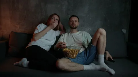 Couple switches channels on the TV while sitting at home and eating popcorn Stock Footage 229692102