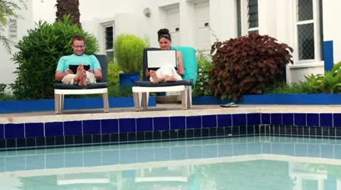 Couple with tablet computer and laptop relaxing on sunbeds, dolly shot Vídeos de archivo 10848817