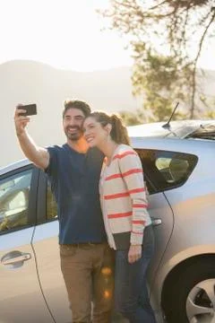 Couple taking self-portrait with camera phone outside car Stock Photos