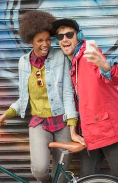 Couple taking self-portrait with cell phone against graffiti wall Stock Photos