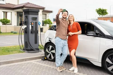 Couple Taking Selfie While Charging Electric Car At Station Stock Photos