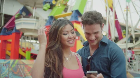 A couple taking selfies in front of a ferris wheel Stock-Footage 55609806