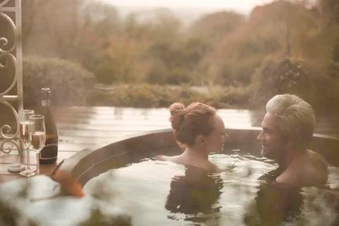 Couple talking soaking in hot tub with champagne on autumn patio Stock Photos