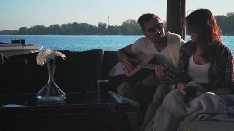 Couple talking while man is holding guitar by the river Stock Footage 99976092