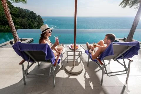 Couple tasting tropical drinks while sitting on sun lounger Stock Photos