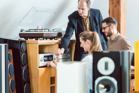 Couple testing a Hi-Fi system in the store with the salesman explaining Stock Photos