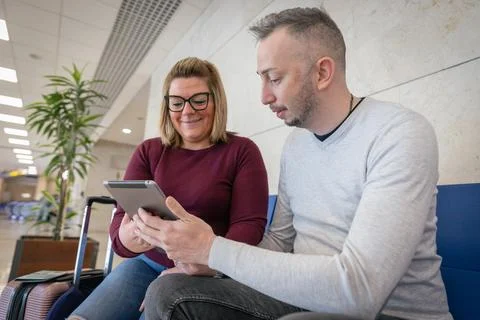 A couple of tourists use a tablet while at the airport ready to travel Foto stock