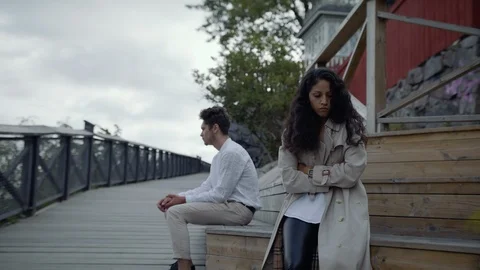 A couple on a tree bench after a fight. The young woman glancing at boyfriend. Stock Footage 115576382
