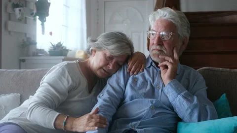Couple of two sad and depressed old people sitting on the sofa at home looking o Stock Footage