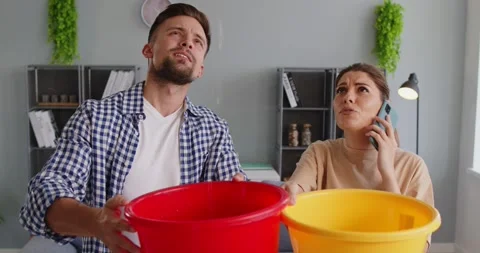 Couple with umbrella catching ceiling leak at home, calling for emergency repair Stock Footage 330702126
