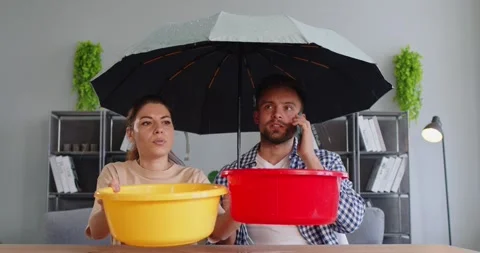 Couple with umbrella catching ceiling leak at home, calling for emergency repair Stock Footage 331247085