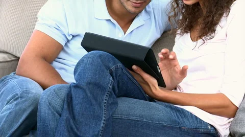 Couple using a computer tablet sitting on the sofa Stock Footage