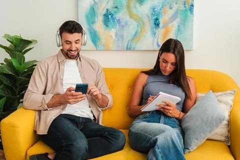 Couple using devices on sofa engage with smartphone and notebook in a cozy Fotos de archivo