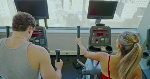 Couple Using Elliptical Machines in High-Rise Gym Stock Footage 323777199