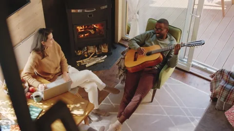 Couple Using Laptop and Playing the Guitar by Fireplace Vídeo Stock 144662772