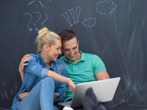 Couple using laptop in front of gray chalkboard happy young loving couple ... Stock Photos